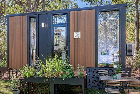 A modern, compact structure with a glass door and windows, surrounded by greenery and outdoor seating. - Peaceful Tiny House Retreat with Garden Pavilion near Armadale, Bedfordale WA (Bedfordale)