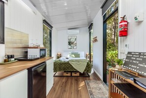 A compact room with a bed, a small kitchenette, and a view of greenery outside. - Peaceful Tiny House Retreat with Garden Pavilion near Armadale, Bedfordale WA (Bedfordale)