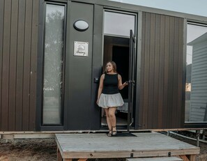 A person standing at the entrance of a modern building with a wooden exterior and a door with a glass panel. - Cozy Secluded Tiny House in Warialda, New South Wales (Warialda)
