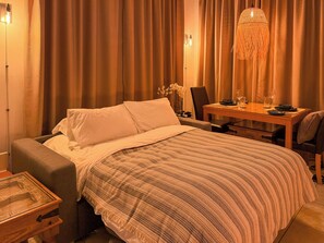 A hotel room with a bed, a desk, a chair, and a dining table set for two. - Sabai Pafos | Stylish Poolside Apartment with Sea View & Two Sunny Terraces (Pafos)