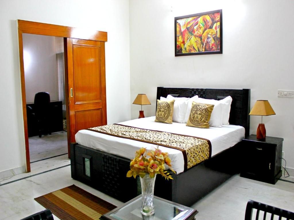 A hotel room with a bed, bedside lamps, a painting on the wall, and a vase with flowers on the table.