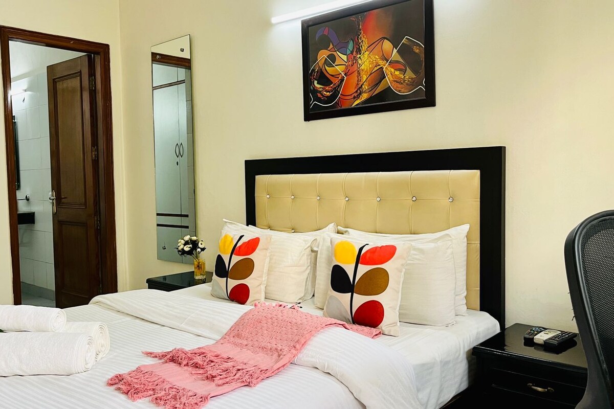 A hotel room with a bed, a nightstand, a chair, a mirror, and a painting on the wall.