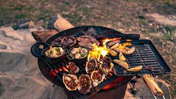 A grill with seafood, meat, and vegetables being cooked outdoors.
