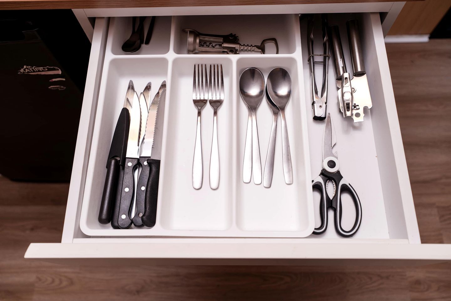 A drawer with utensils, including knives, forks, spoons, and scissors, organized in compartments.