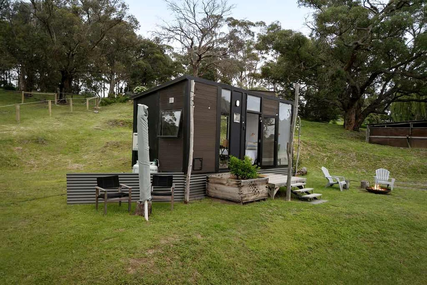 A small, modern cabin with a deck, seating area, and a fire pit.