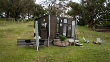 A small, modern cabin with a deck, seating area, and a fire pit.