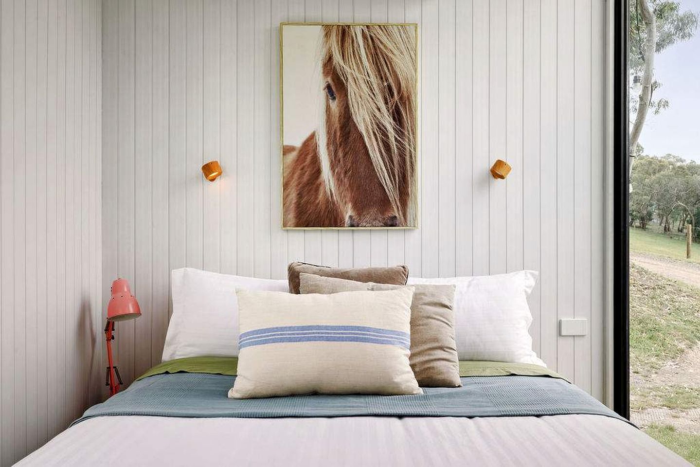 A bedroom with a bed, pillows, a lamp, and a wall-mounted picture.