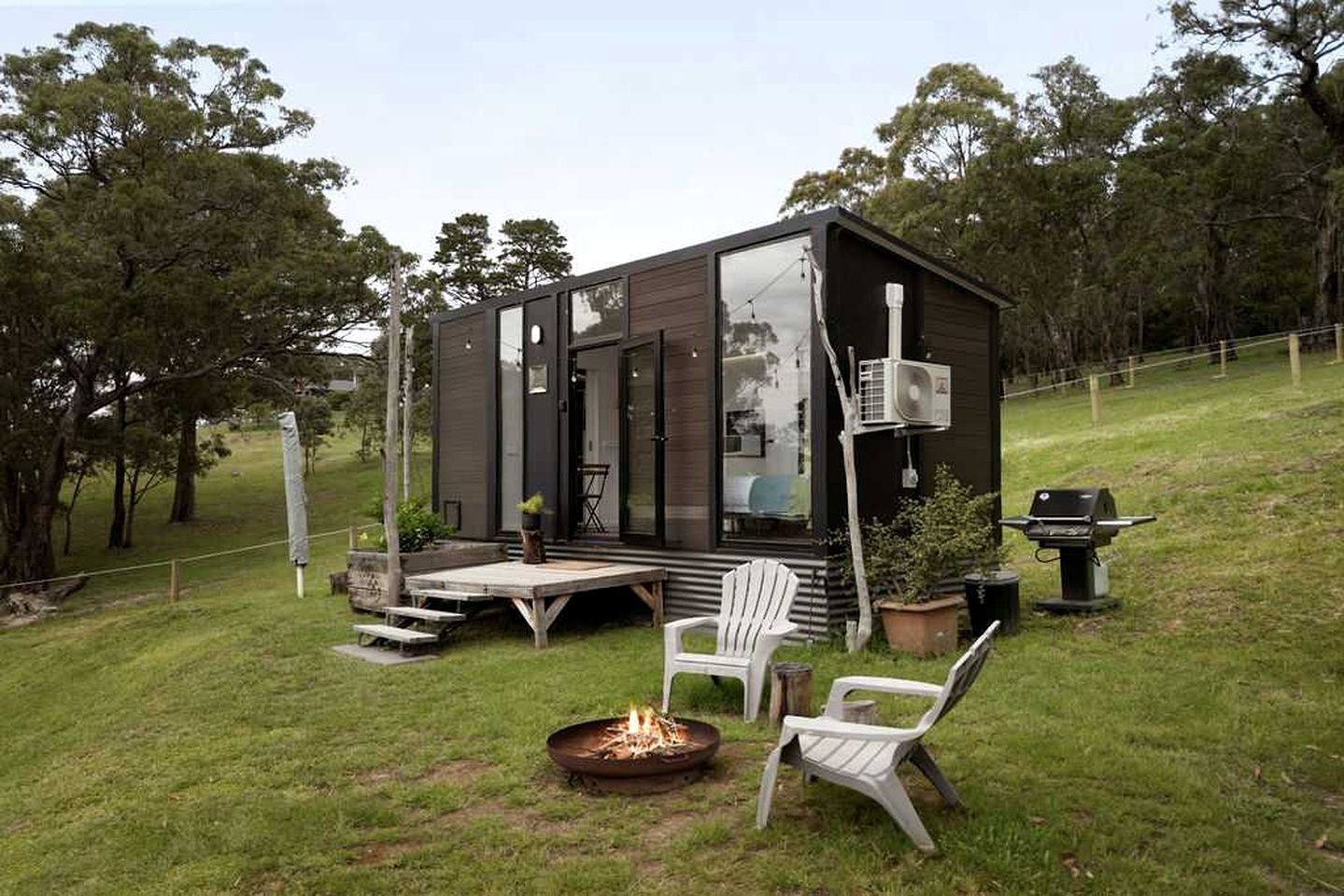 A modern cabin with a deck, outdoor seating, and a fire pit.