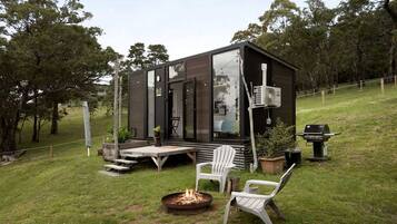 A modern cabin with a deck, outdoor seating, and a fire pit.
