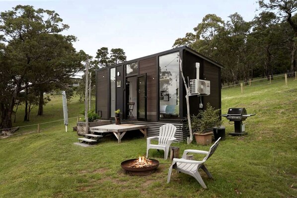 A modern cabin with a deck, outdoor seating, and a fire pit.