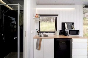 A compact kitchen with a window, a sink, a microwave, and a dishwasher. - Acre Away in Hurstbridge, Victoria (Hurstbridge)