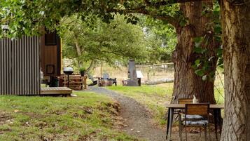 A rustic outdoor seating area with a wooden table and chairs, a grill, and a small shed.