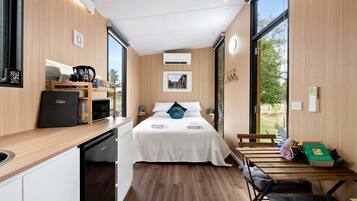 A compact room with a bed, a small kitchenette, and a view through a large window.