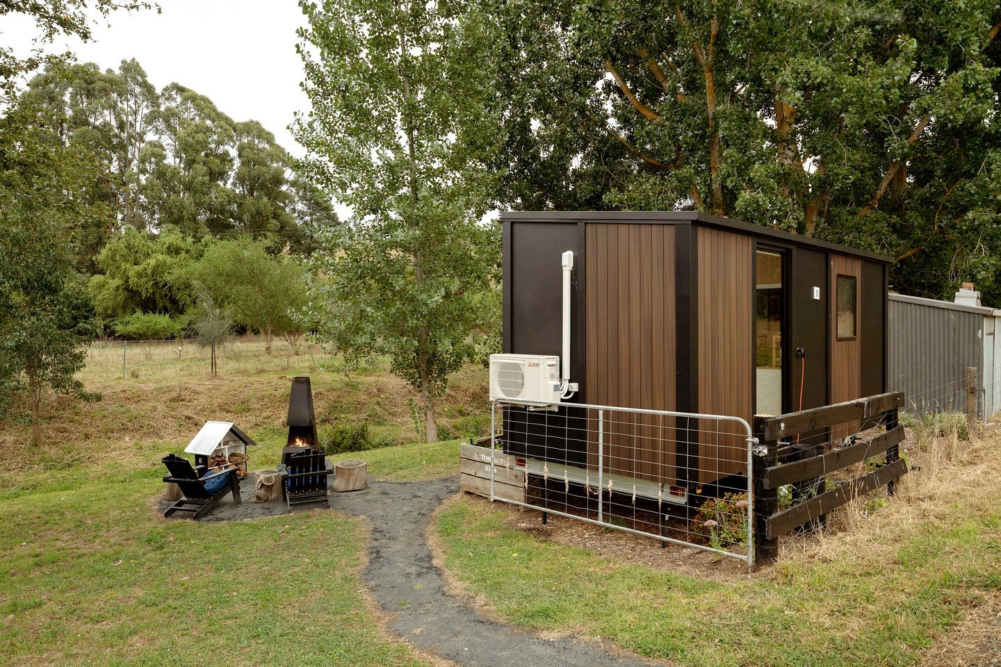 A small, single-story cabin with a metal fence, a fire pit, and a portable grill.