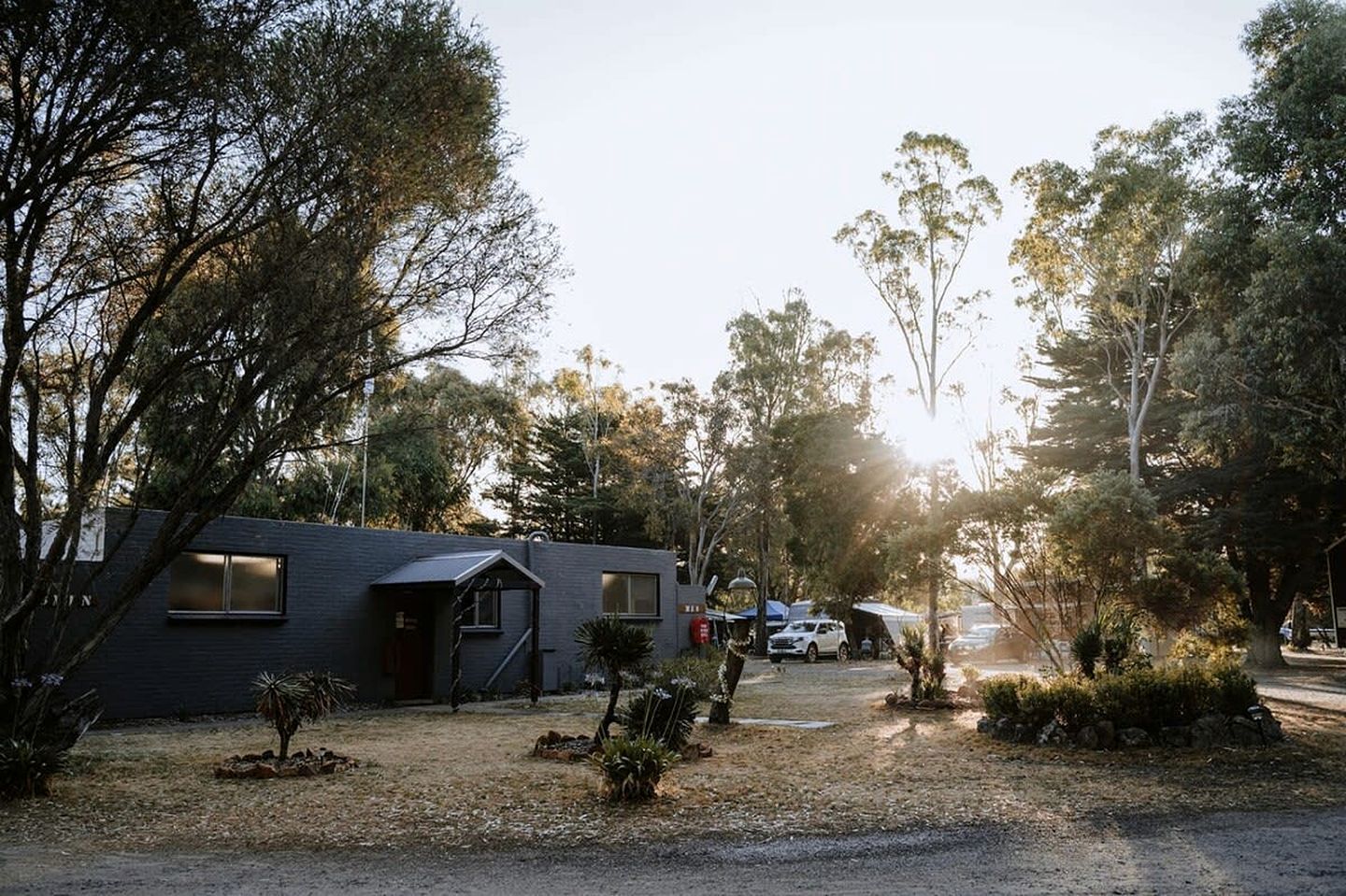 A modern building with a dark facade, surrounded by trees and a gravel driveway.