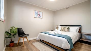Een slaapkamer met een bed, een stoel, een plant in een pot en een kunstwerk aan de muur.