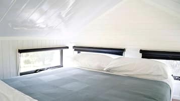 A bedroom with a bed, two windows, and a sloped ceiling.