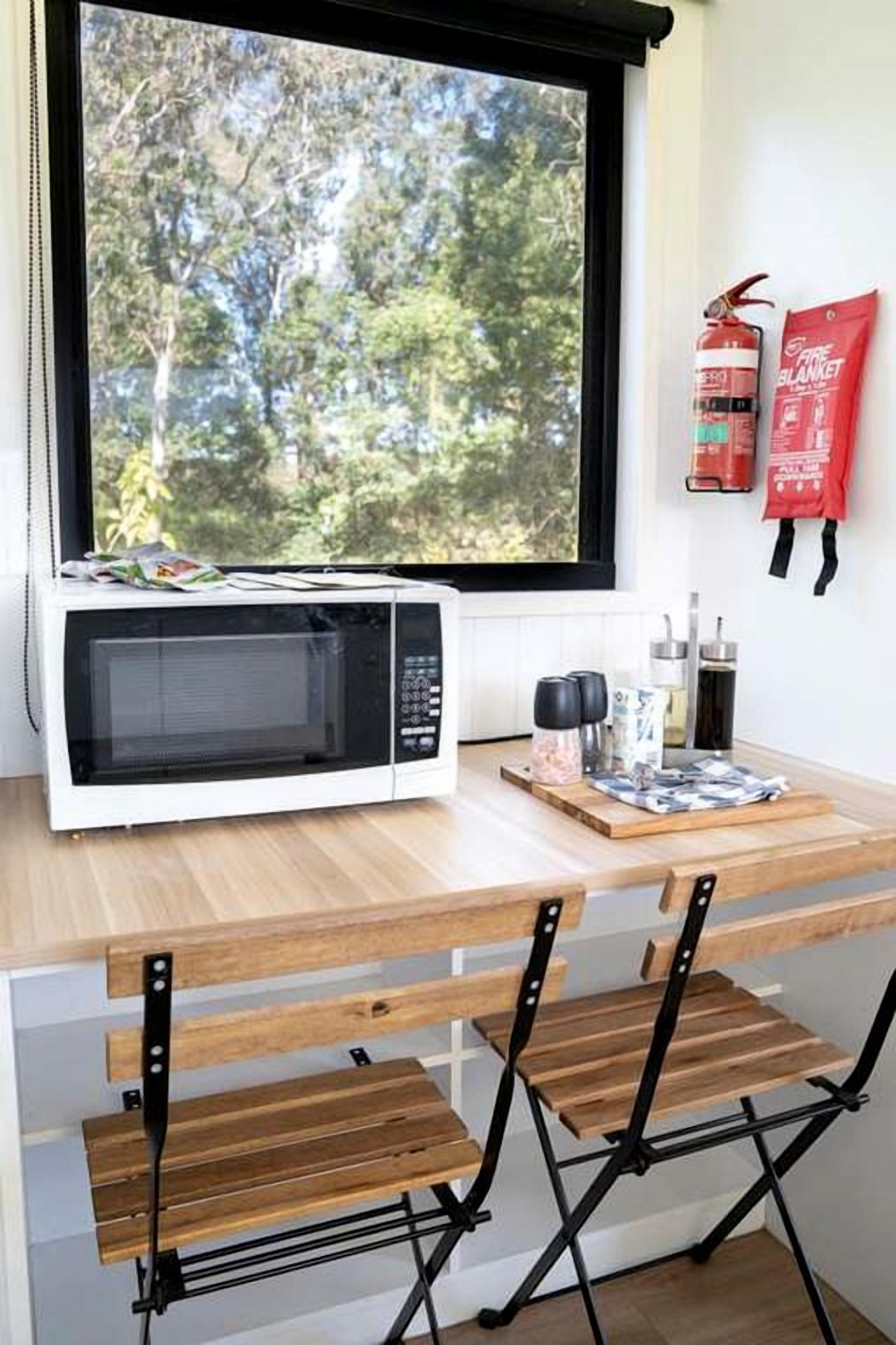 A kitchen with a microwave, a window with a view of trees, and a fire extinguisher on the wall.