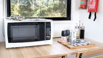 A kitchen with a microwave, a window with a view of trees, and a fire extinguisher on the wall.