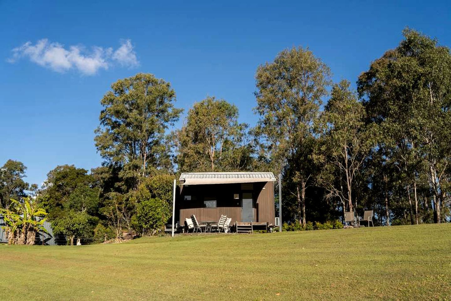 A single-story building with a flat roof, surrounded by a grassy field and tall trees.