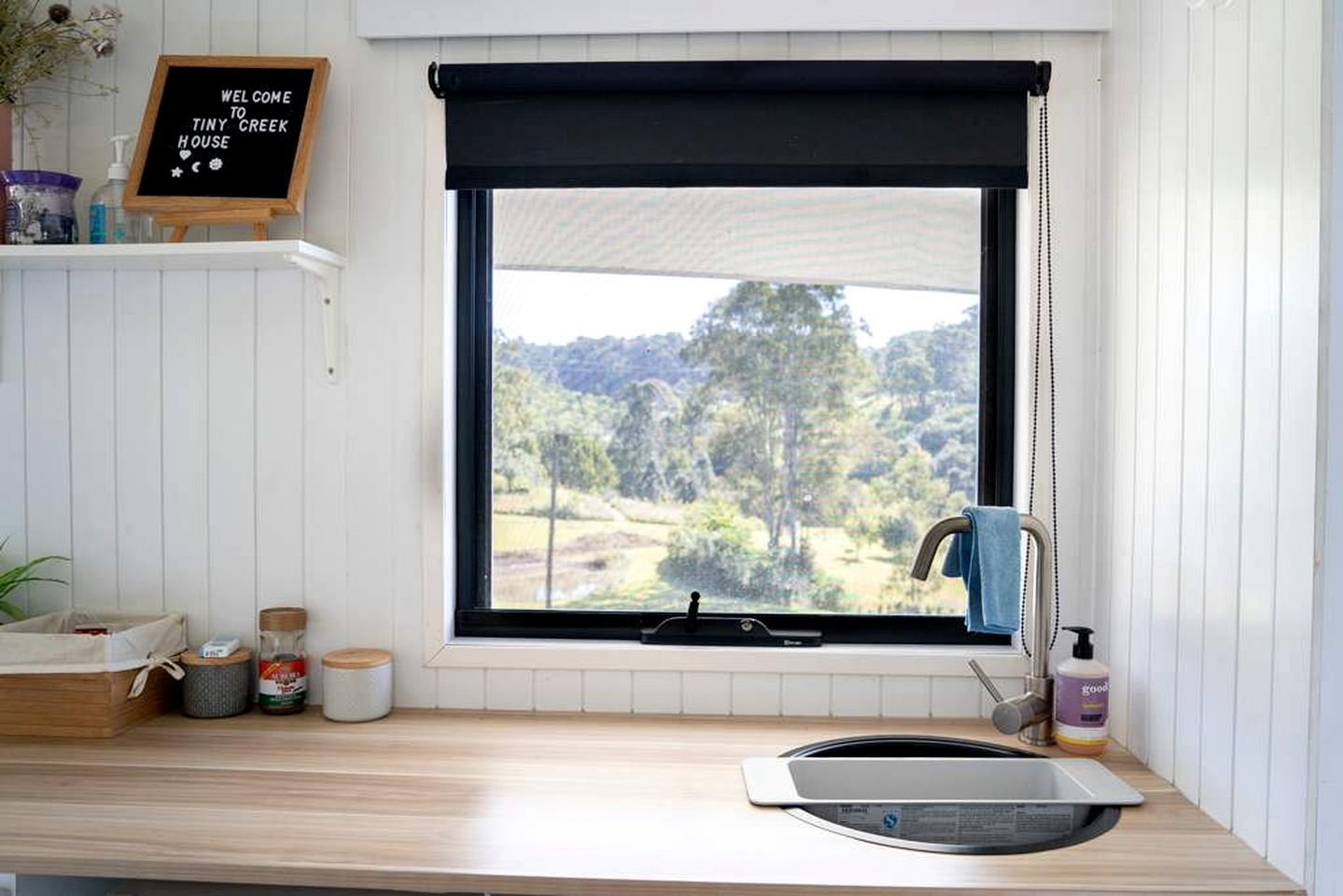 A kitchen with a window, a blackboard sign, a sink, and a towel hanging on the door.