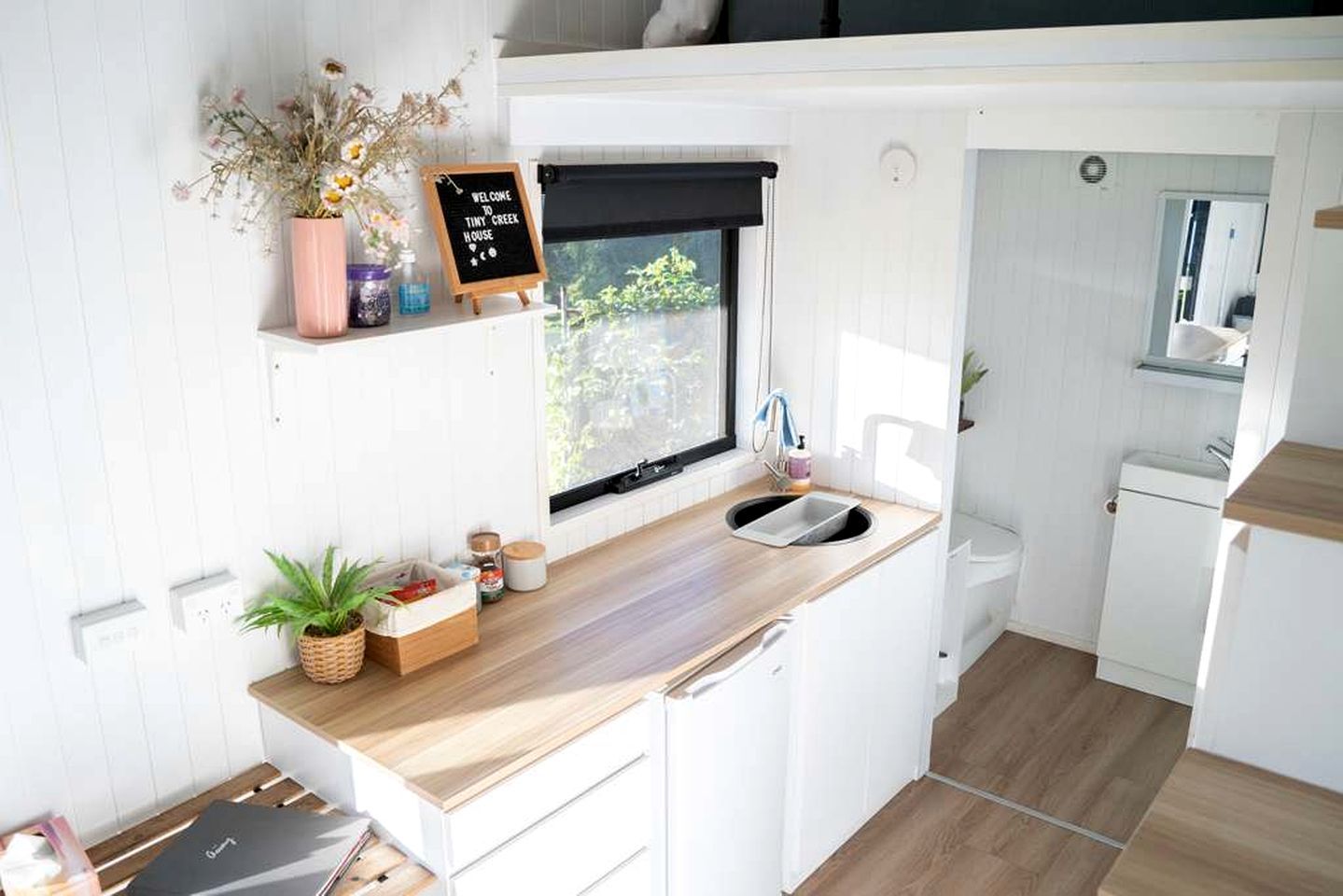 A compact kitchen with a wooden countertop, a blackboard sign, and a window with a view.