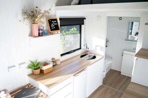 A compact kitchen with a wooden countertop, a blackboard sign, and a window with a view. - Sunshine Coast Tiny Home for Glamping in Queensland (Perwillowen)