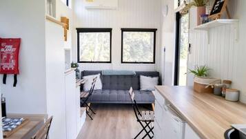 A compact kitchen with a grey sofa, wooden dining table, and a red fire blanket.