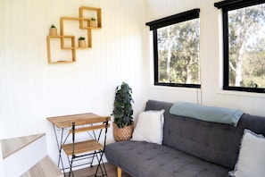 A room with a grey sofa, a wooden table, and a window with a view of trees.