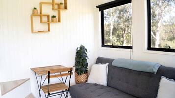 Una habitación con un sofá gris, una mesa de madera y un ventanal con vista a árboles.