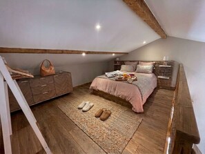 Une chambre avec un lit en mezzanine, un plancher en bois, une table de chevet et une commode.