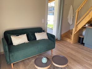 A green sofa with two pillows, a wooden staircase, and a small trash bin. - Les Violettes Des Bastides, maison de charme dans un joli village médiéval. (Cologne)