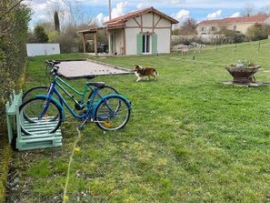 A bicycle parked on a grassy lawn with a dog in the background and a house with a red roof. - Les Violettes Des Bastides, maison de charme dans un joli village médiéval. (Cologne)