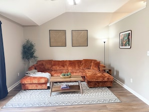 Una sala de estar con un sofá modular, una mesita de centro, un tapete estampado y dos obras de arte colgadas en la pared.