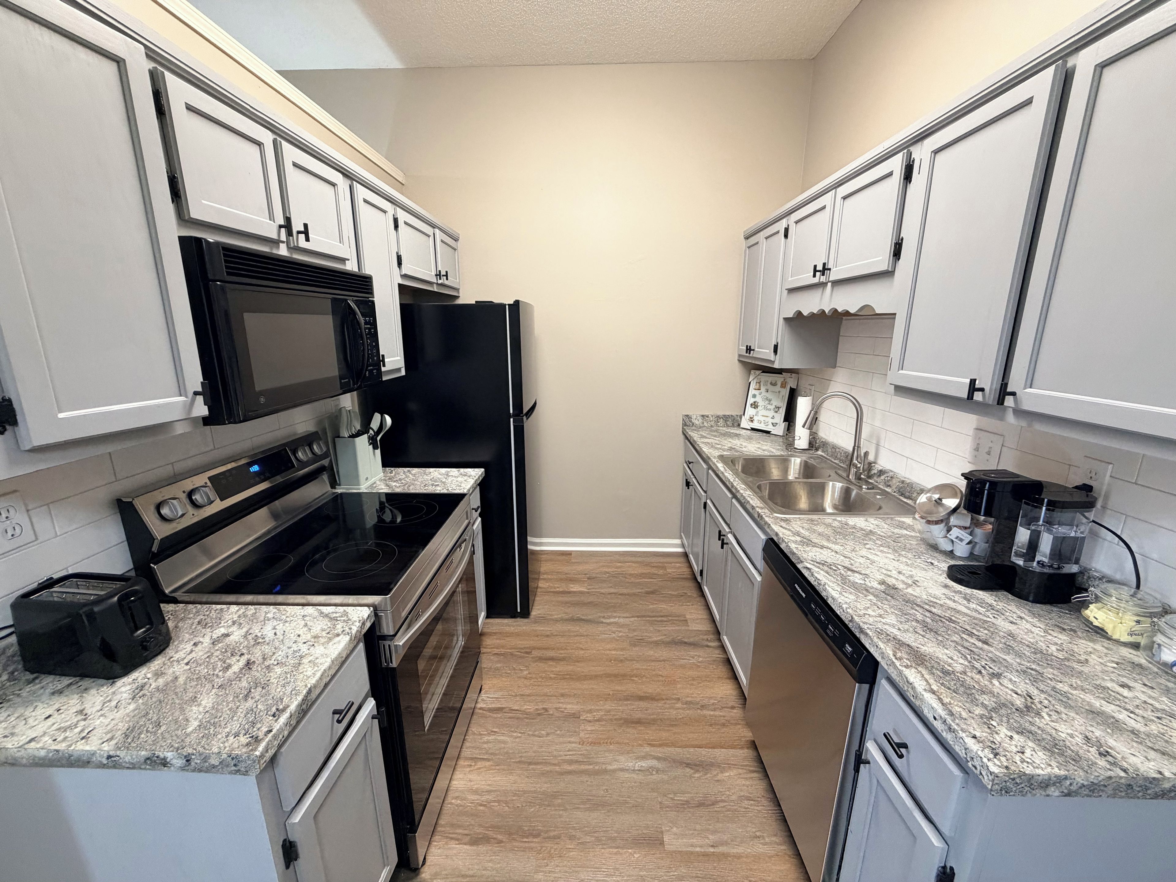 A modern kitchen with white cabinets, a black refrigerator, stainless steel appliances, and a granite countertop.