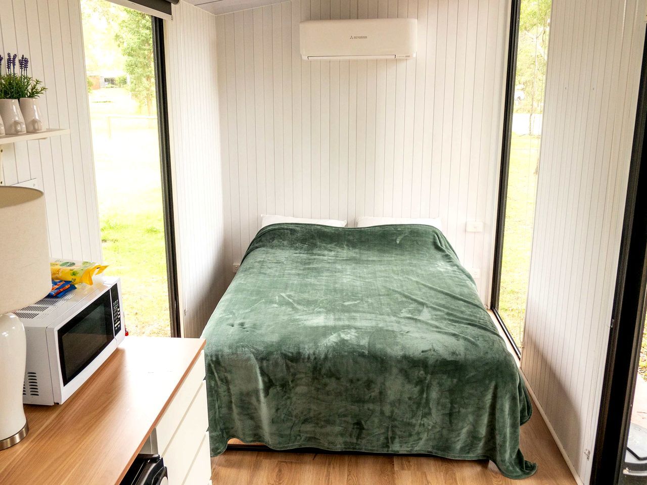Une petite pièce avec un lit, un four à micro-ondes et une fenêtre.