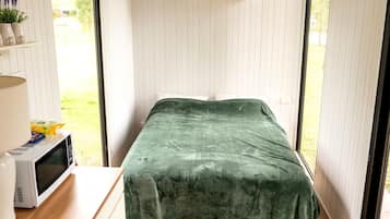 Une petite pièce avec un lit, un four à micro-ondes et une fenêtre.