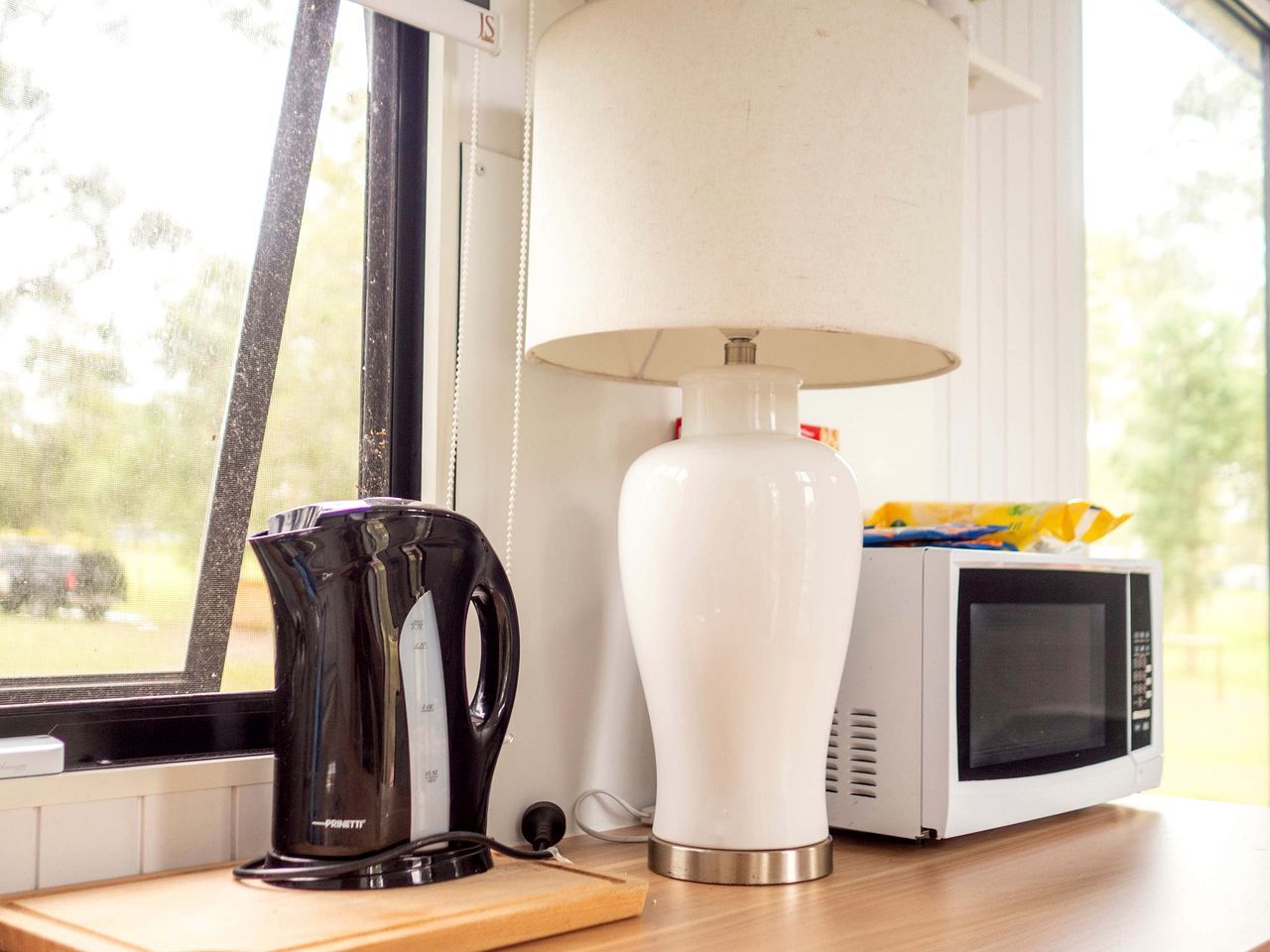 Un coin cuisine comprenant une bouilloire, une lampe et un four à micro-ondes, le tout posé sur un plan de travail en bois.