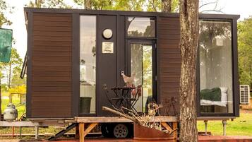 Une petite cabane moderne dotée d’une porte coulissante, d’une fenêtre et d’un petit espace extérieur avec une table et des chaises.