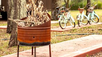 A rustic planter with dried plants on a metal stand, a pathway, and bicycles parked in the background.