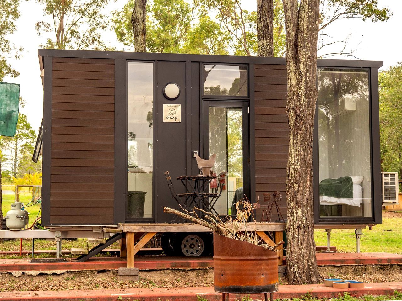 Une petite cabane moderne dotée d’une porte coulissante, d’une fenêtre et d’un petit espace extérieur avec une table et des chaises.
