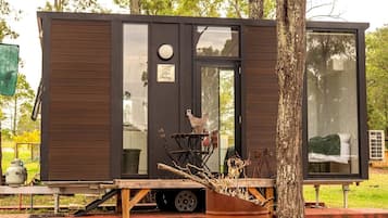 Une petite cabane moderne dotée d’une porte coulissante, d’une fenêtre et d’un petit espace extérieur avec une table et des chaises.