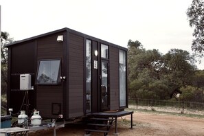 A compact, dark-colored cabin with a sliding glass door, a small porch, and a visible propane tank. - Beautiful Tiny House Near Turquoise Waters and Outdoor Living in Western Australia, Australia (Ellenbrook)