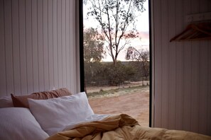 A bedroom with a bed, pillows, and a view of a tree and fence through a window. - Beautiful Tiny House Near Turquoise Waters and Outdoor Living in Western Australia, Australia (Ellenbrook)