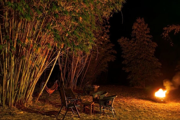 A campsite at night with a fire, chairs, and a table.