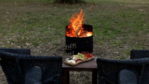 Een terras met een vuurkorf, twee rieten stoelen en een houten tafel met eten en drinken.