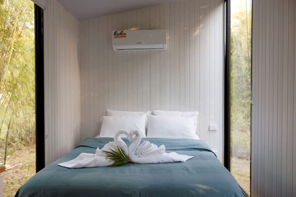 Habitación de hotel con cama, almohadas blancas, colcha color esmeralda y una decoración de toallas con forma de cisne.