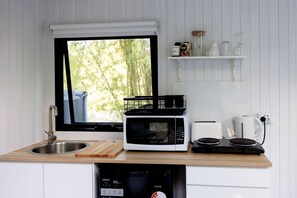 Cocina compacta con lavamanos, microondas, tostadora, hervidor y ventana con vista a la vegetación.