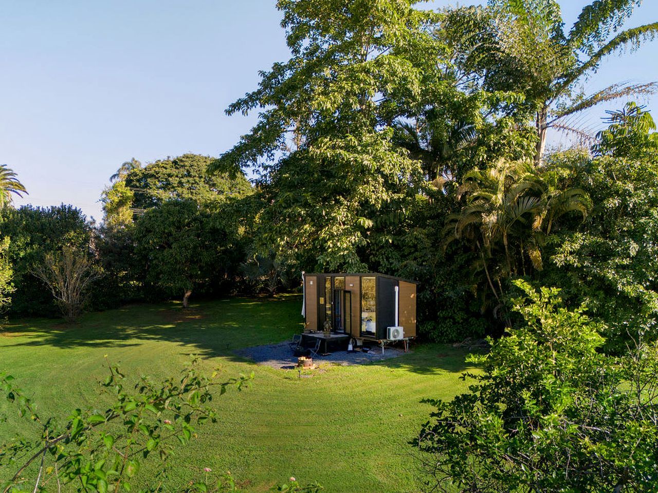 Une petite construction indépendante, dotée d’une porte et de fenêtres, entourée d’une végétation luxuriante et d’arbres.