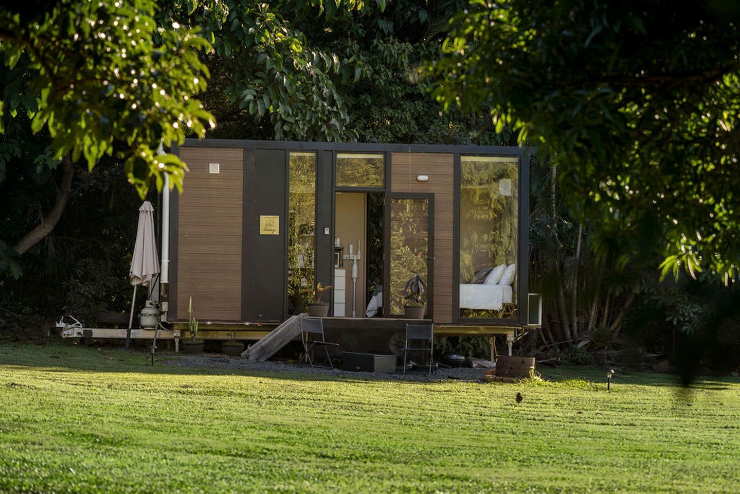 Une petite cabane moderne, avec une façade en bois, une porte en verre et un petit espace porche.